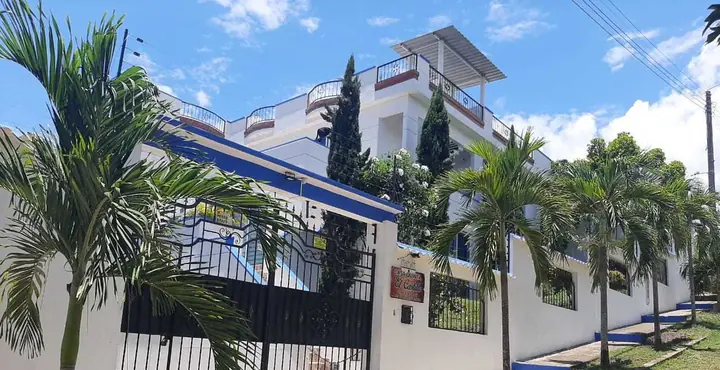 Fachada blanca con remates azules y palmas bajo el cielo de Melgar